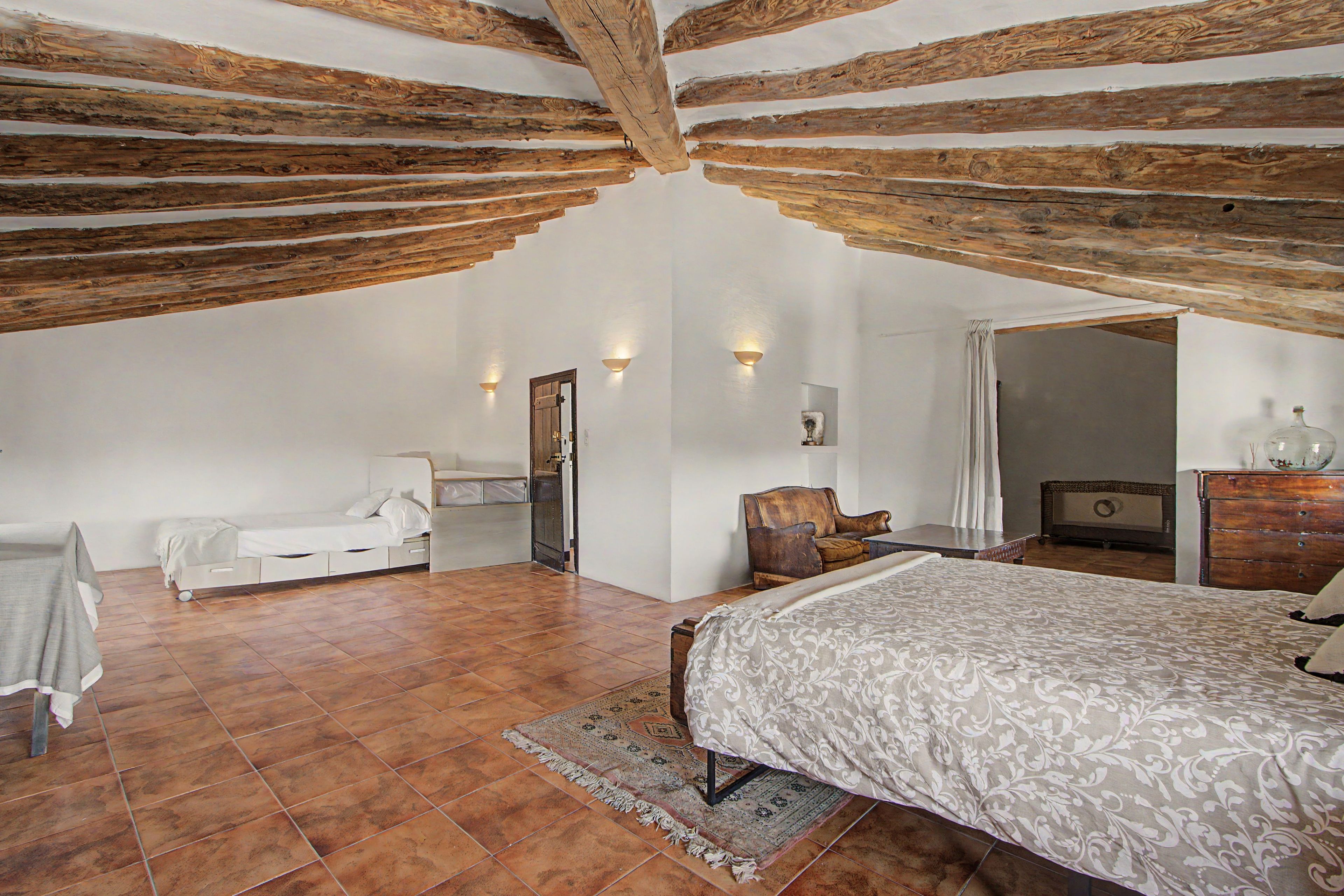 A bedroom with a sloped ceiling, a bed, a chair, a dresser, and a mirror.