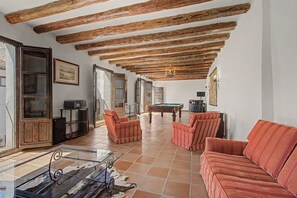Ampla sala de estar com mesa de bilhar, sofás listrados de vermelho e uma mesa de centro de vidro.