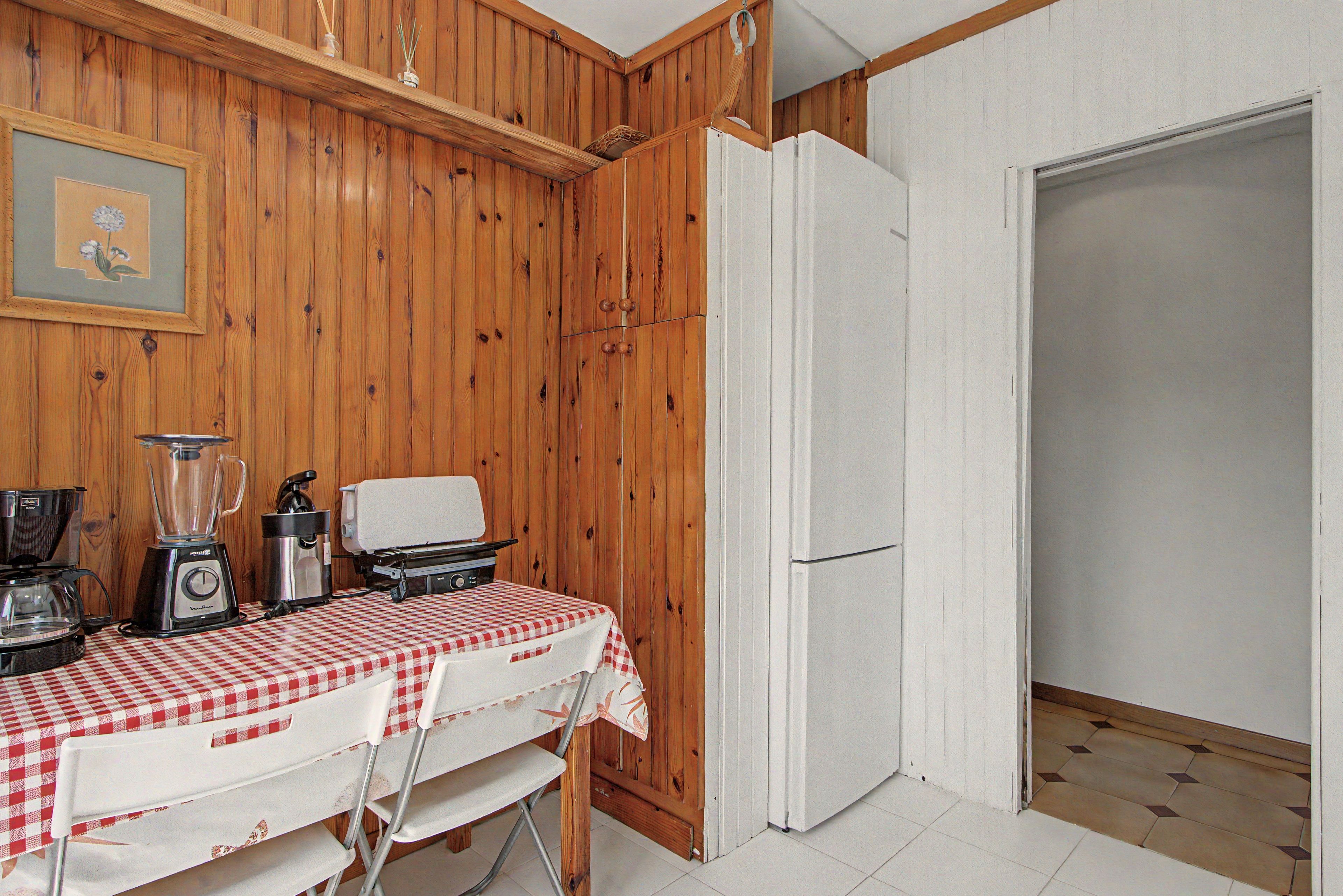 Una cocina con paredes de madera, un refrigerador, una mesa con mantel a cuadros y una licuadora.