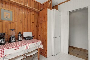 Uma cozinha com paredes de madeira, uma geladeira, uma mesa com toalha xadrez e um liquidificador.