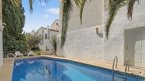 Una piscina con superficie de agua azul cristalina, rodeada por un muro blanco y palmeras.