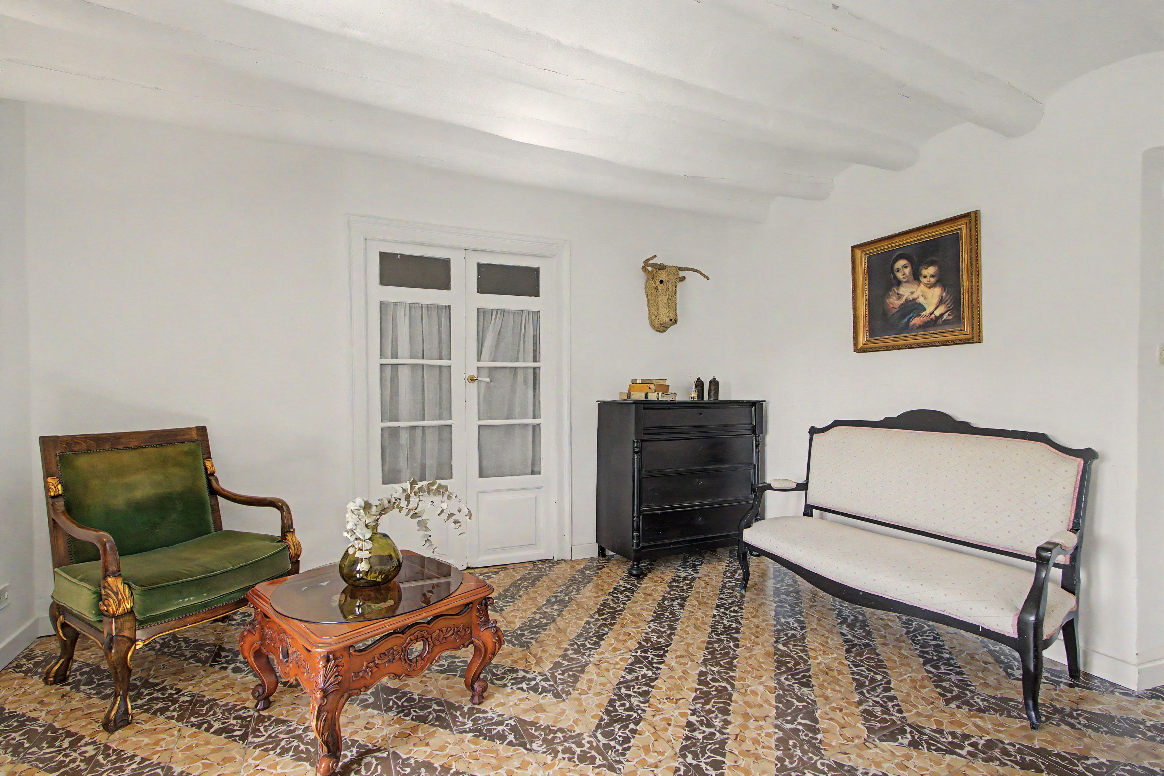 Una habitación con un sillón verde, un sofá blanco, una mesa de centro de madera con un jarrón, un mueble negro y un cuadro colgado en la pared.