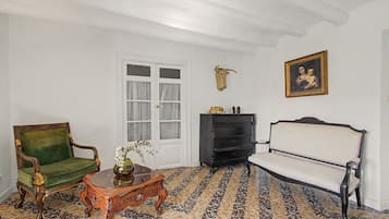 Una habitación con un sillón verde, un sofá blanco, una mesa de centro de madera con un jarrón, un mueble negro y un cuadro colgado en la pared.