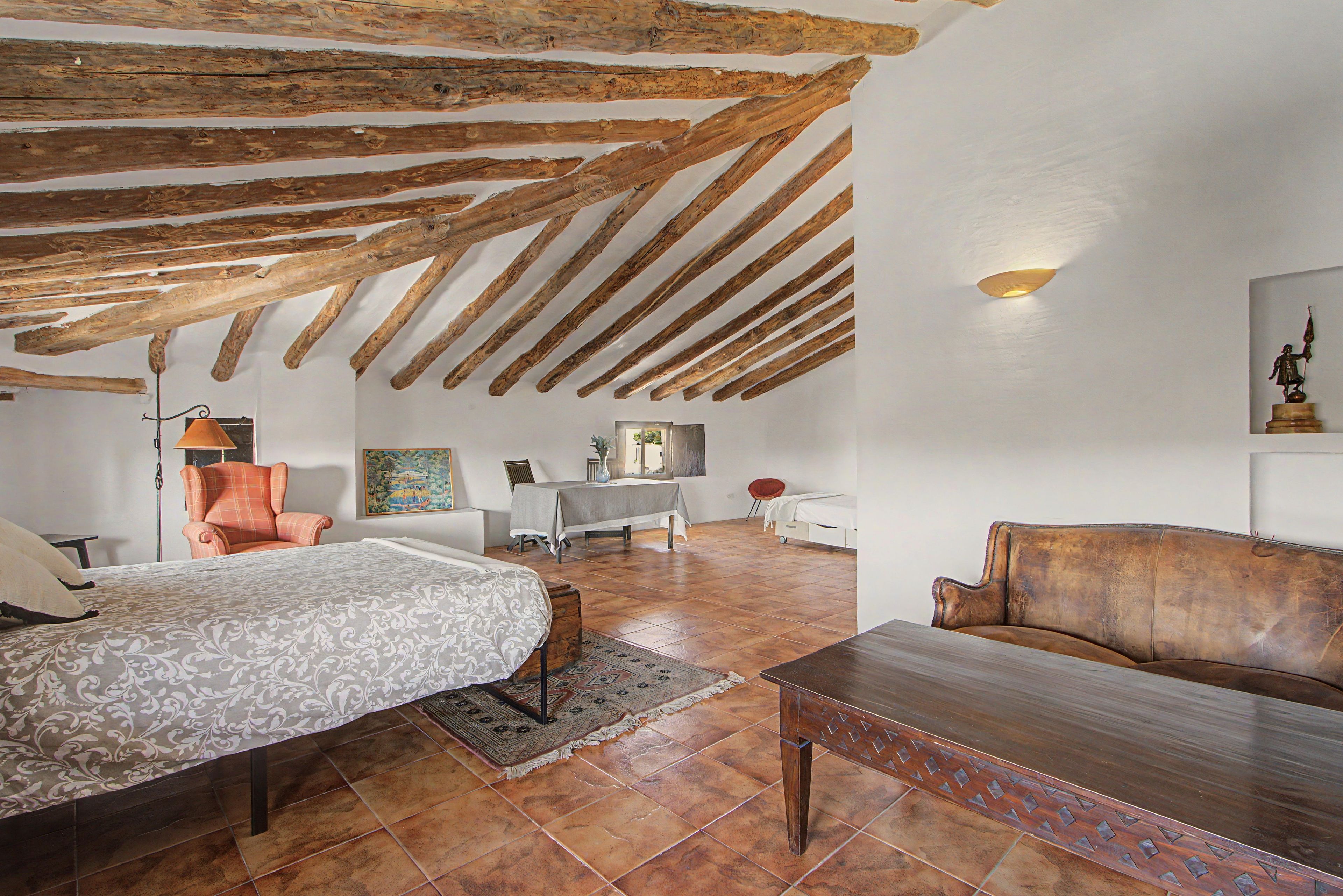 Une pièce avec des poutres apparentes, un lit, un canapé, une table et une chaise.