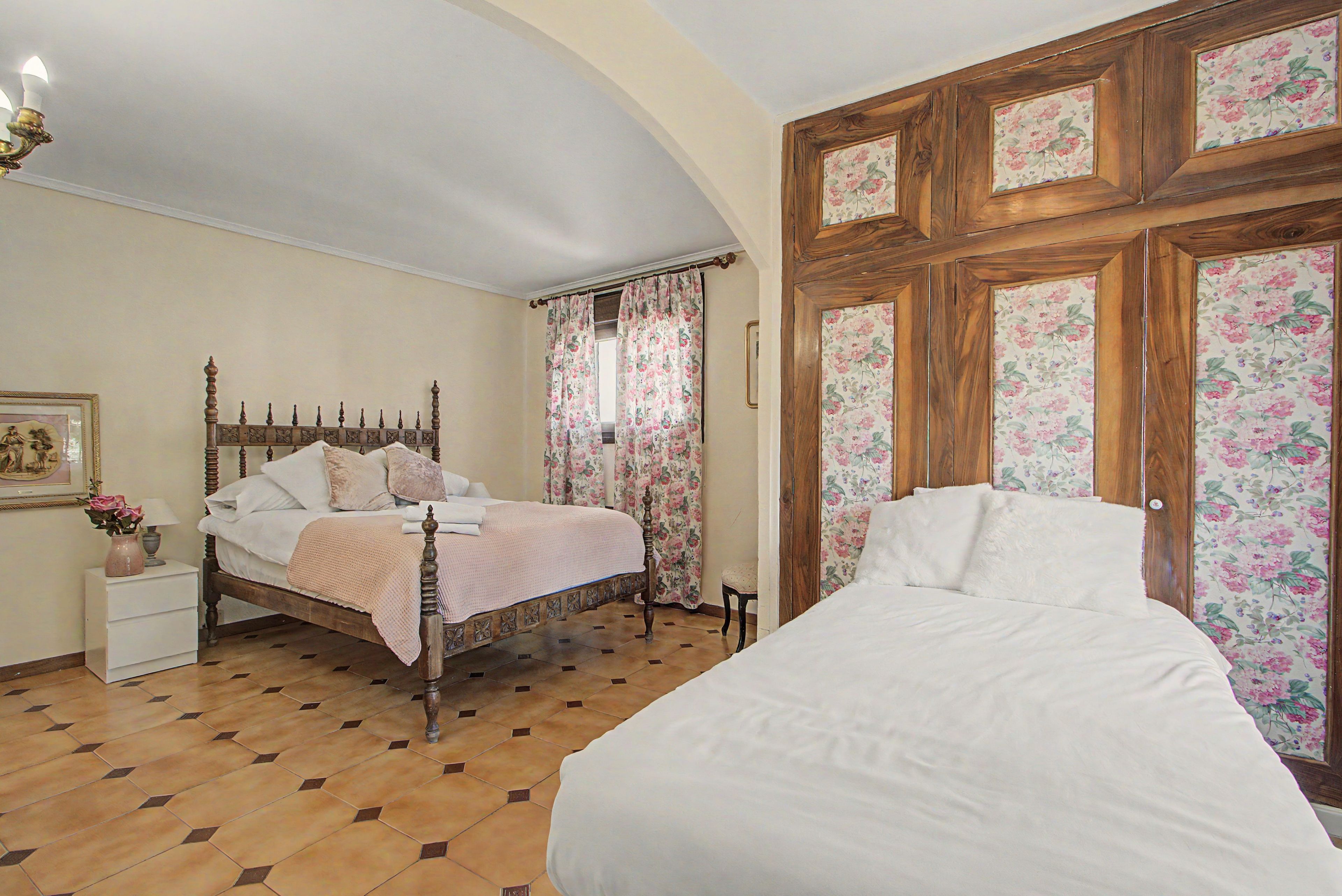 Ein Schlafzimmer mit einem hölzernen Bett, einem zusätzlichen Bett, einem Nachttisch mit Lampe und einem Sessel.