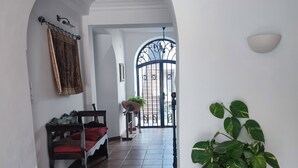 A hallway with a tiled floor, a potted plant, a bench, and a door with a wrought iron gate.