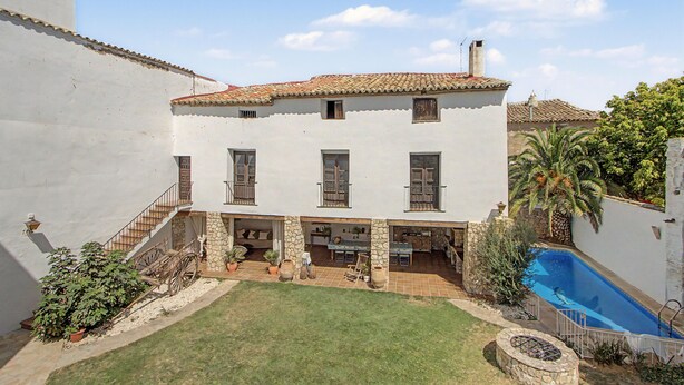 Una casa de dos pisos con techo de tejas, piscina y un pequeño jardín.