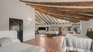 Habitación amplia con techo alto, vigas de madera a la vista, una cama, una mesa y una silla.
