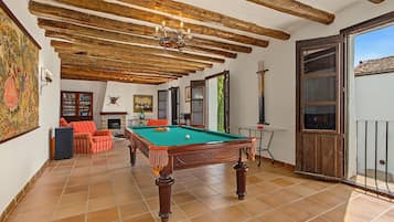 Een ruime kamer met een pooltafel, een open haard en een balkon met uitzicht.