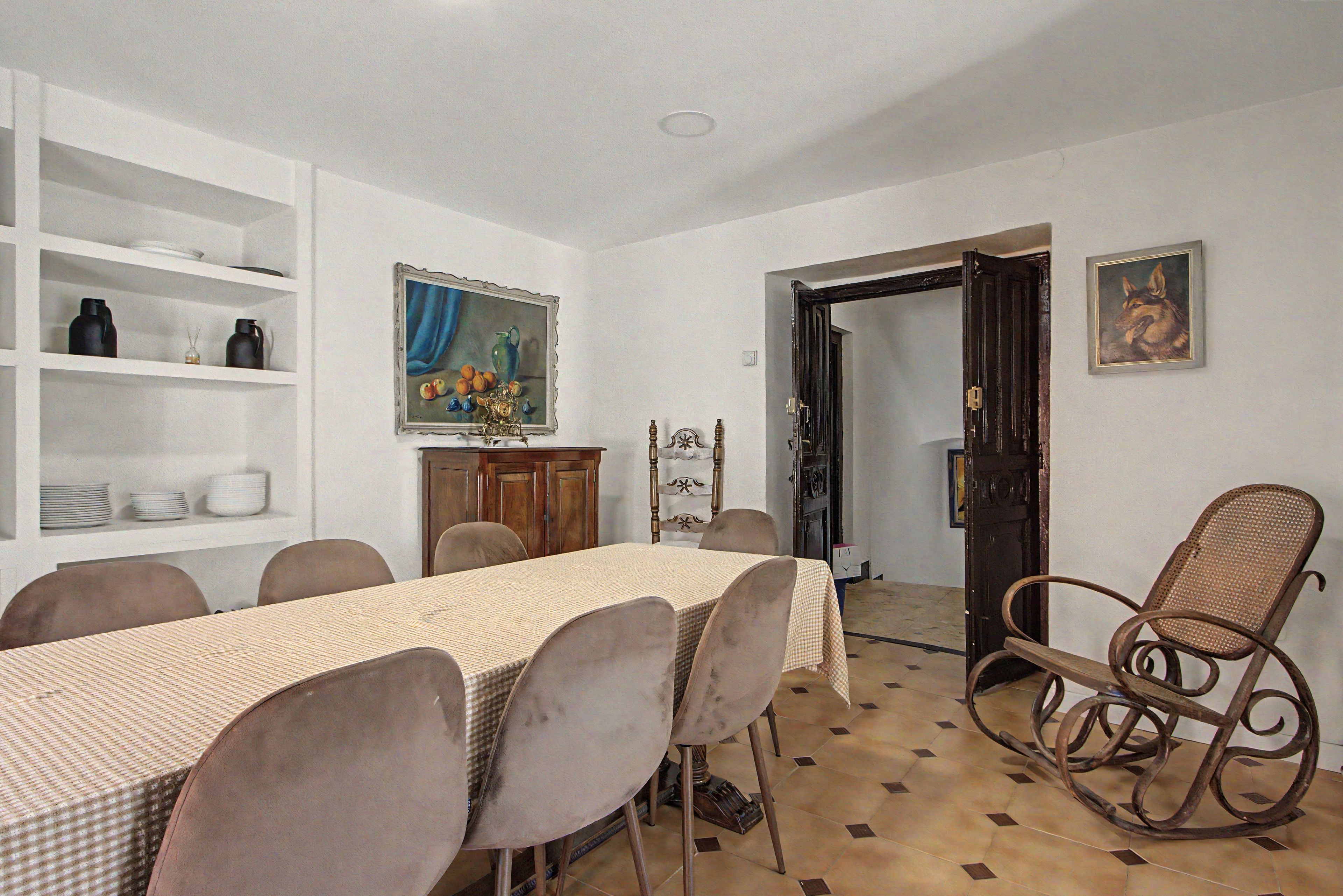 A dining area with a table set for six, surrounded by chairs, a wooden cabinet, and a painting on the wall.