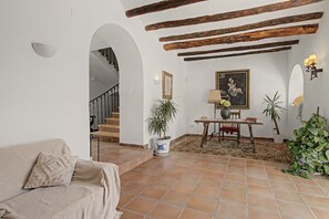 A living room with a sofa, a table with a lamp, a painting, and a staircase leading to another room.