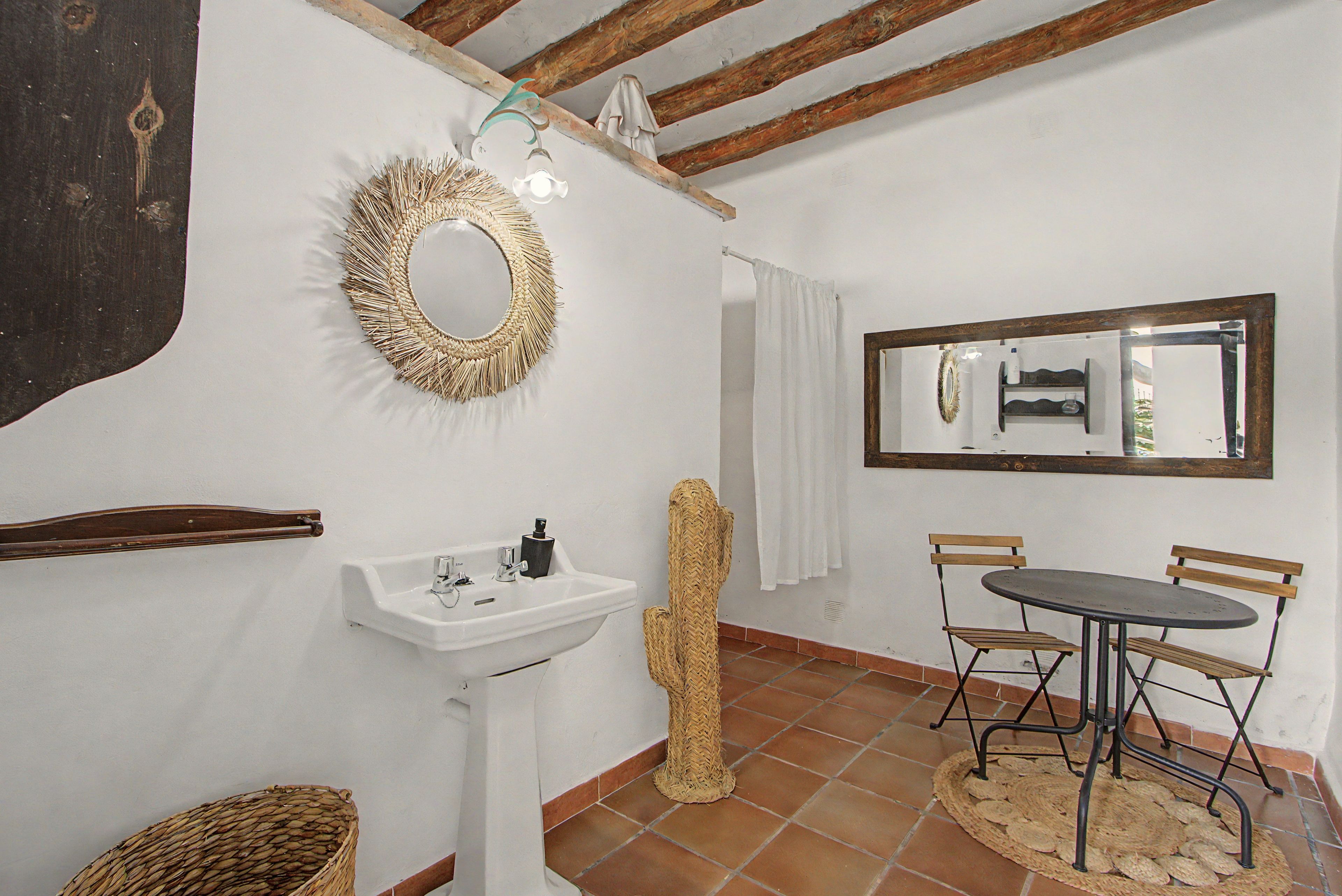 Casa de banho com lavatório branco, espelho, banco de madeira e cesto trançado.