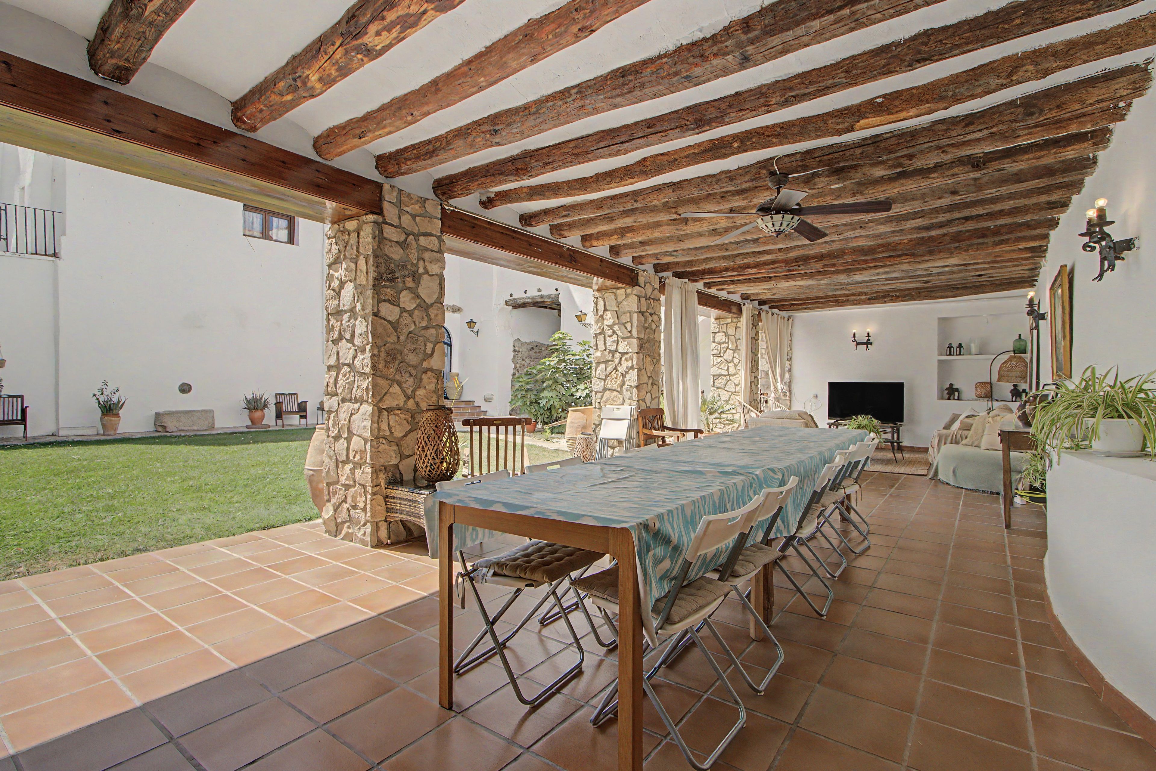 Un patio exterior con una mesa de comedor y sillas, pilares de piedra y un ventilador de techo.