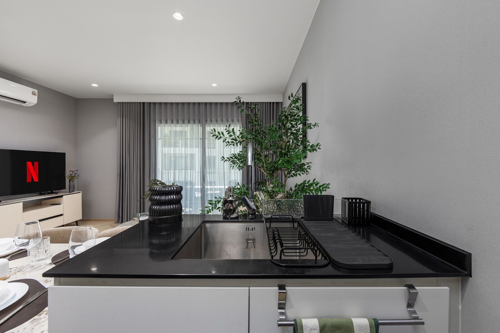 A modern kitchen with a black countertop, stainless steel appliances, a dining area with a table set for two, and a TV displaying the Netflix logo.