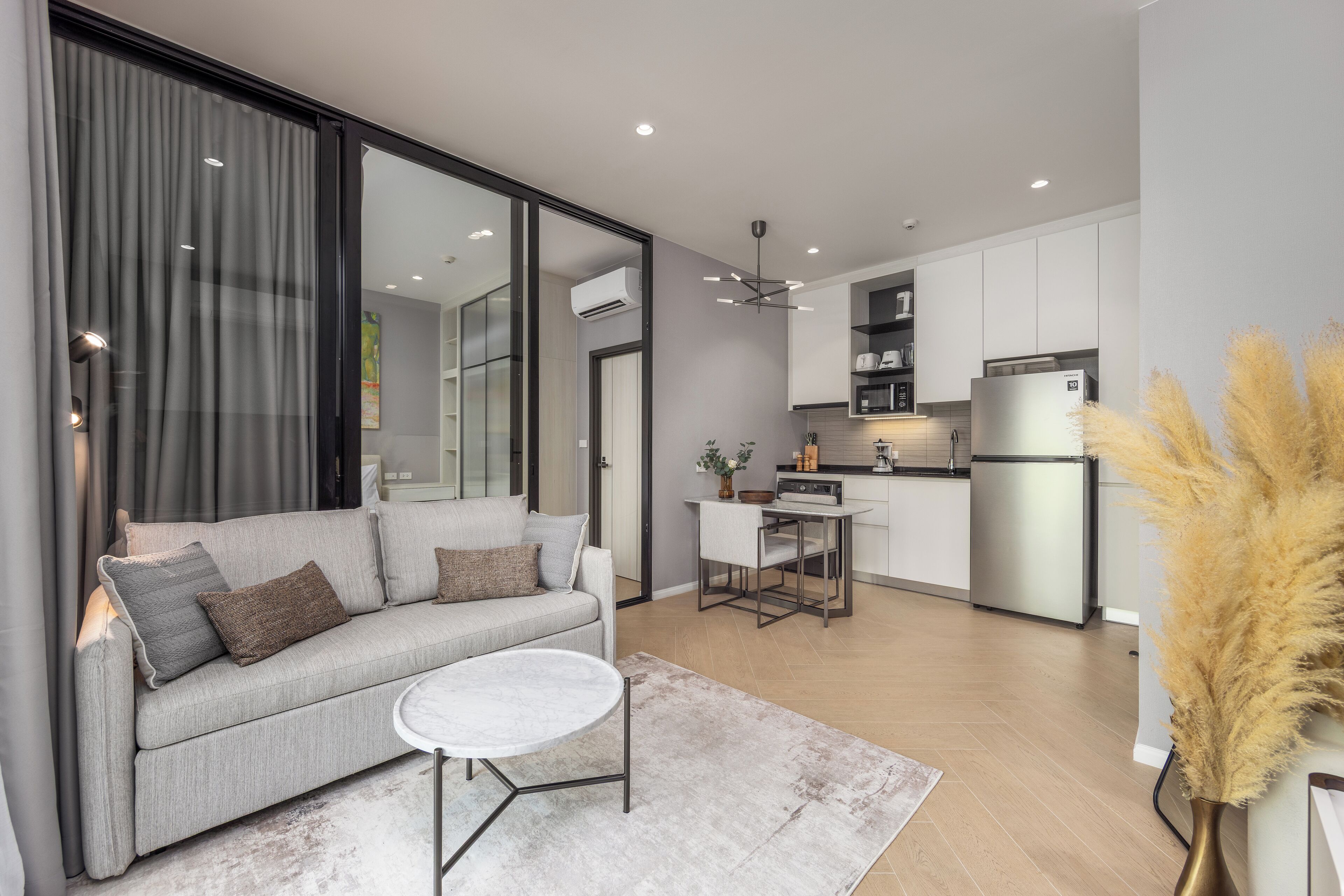 A modern living room with a sofa, coffee table, and a dining area with a small table and chairs. There is a kitchen area with cabinets and appliances.