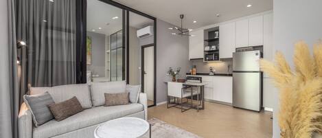 A modern living room with a sofa, coffee table, and a dining area with a small table and chairs. There is a kitchen area with cabinets and appliances.