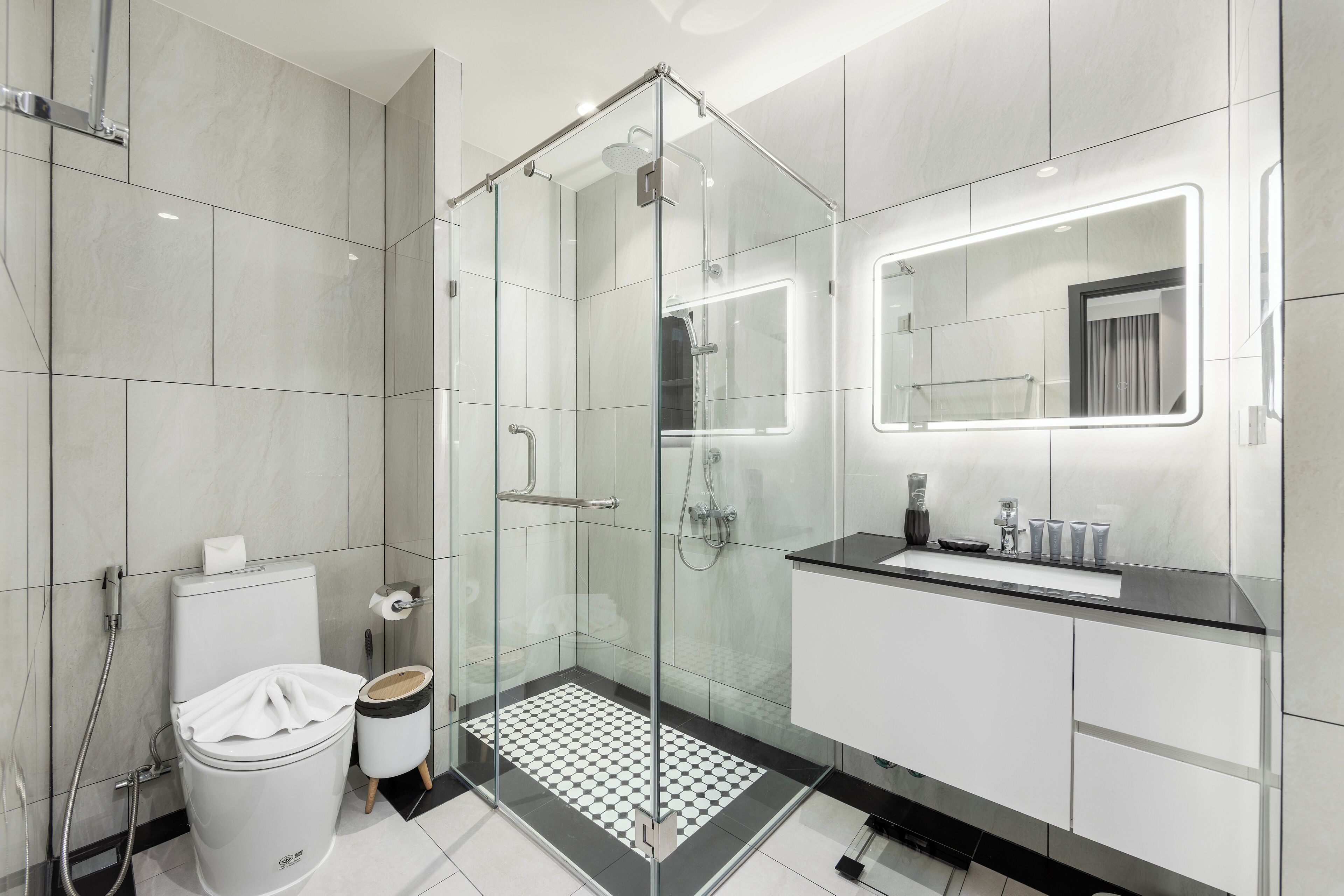 A modern bathroom with a glass-enclosed shower, a toilet, a sink with a mirror, and a tiled floor.