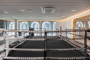 Um ringue de boxe com a marca 'The Title Legendary Bang-Tao', cercado por um interior moderno com grandes janelas e teto alto.