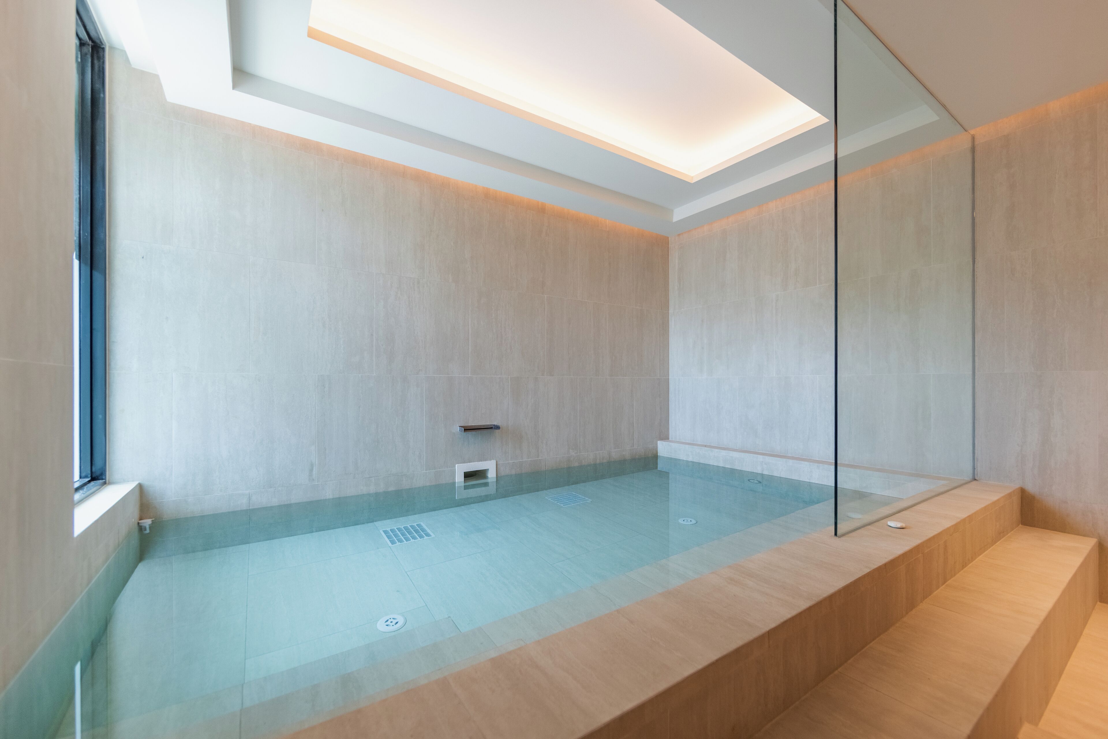 A modern bathroom with a glass-enclosed jacuzzi, light-colored tiles, and a minimalist design.
