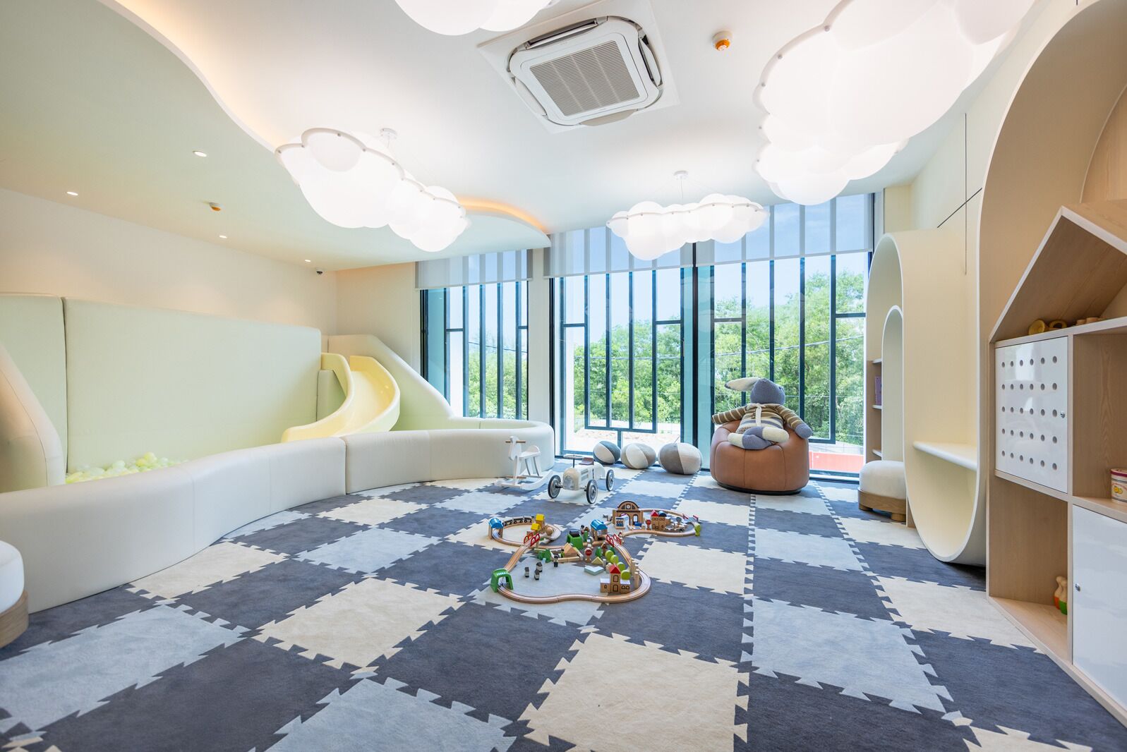 Sala de juegos para niños con tobogán, pufs y una zona de juegos con juguetes y un tren.