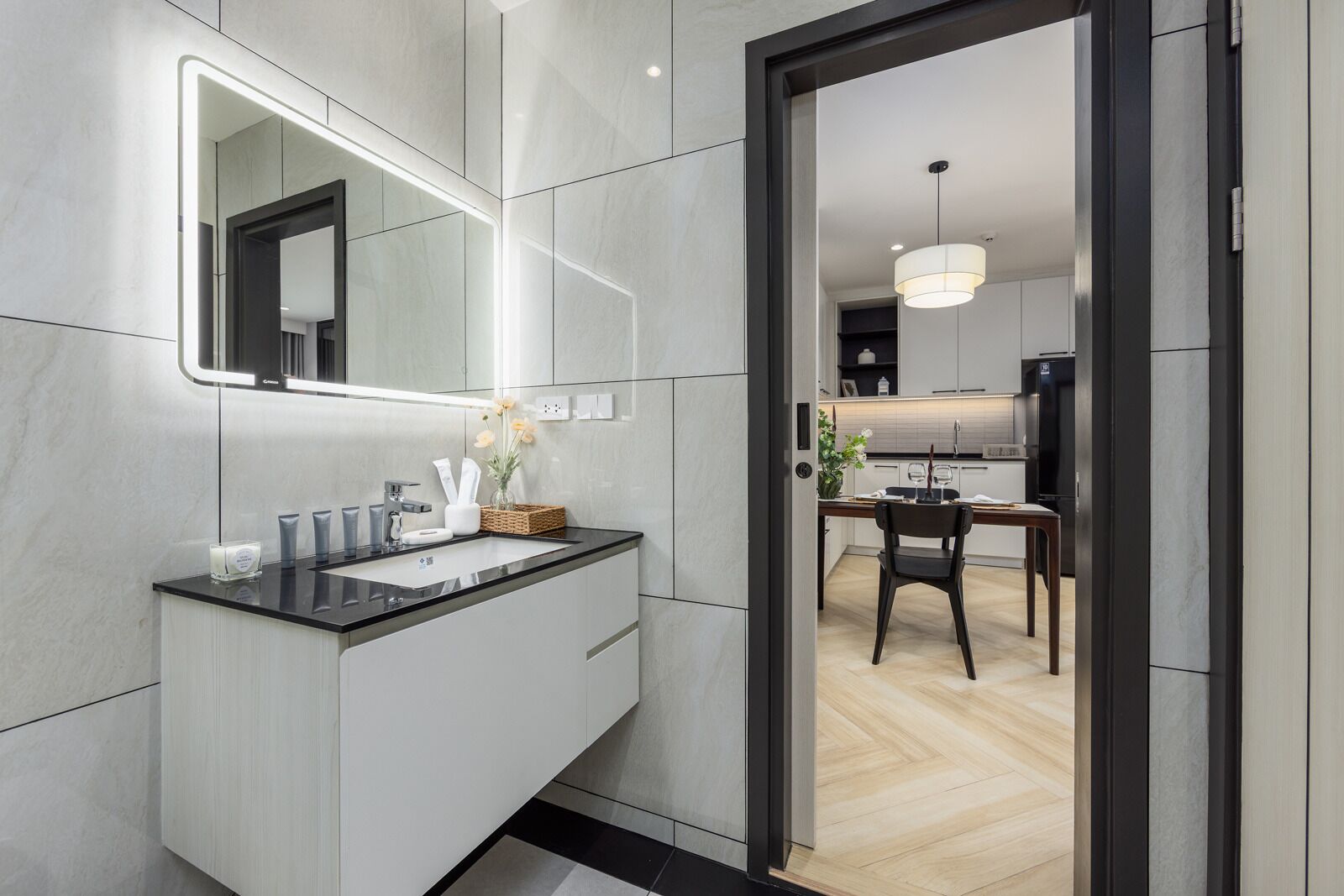 A modern bathroom with a large mirror, a black countertop, and a wooden floor.