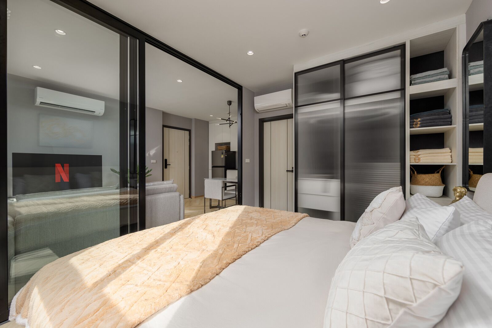 A modern bedroom with a large bed, a glass wall, a wardrobe, and a desk.