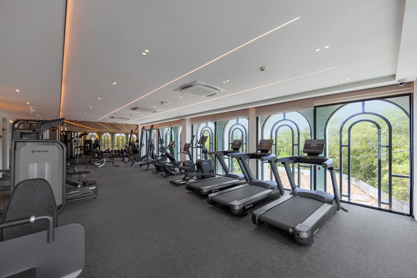 A gym with treadmills, weight machines, and a large window with a view of greenery.