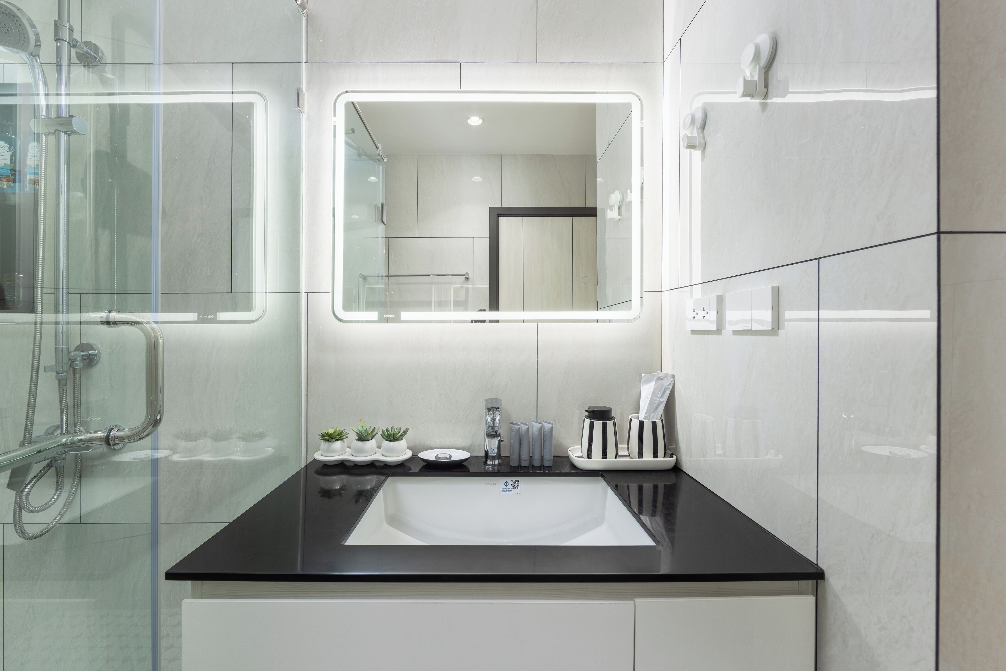 Un bagno moderno con un piano di lavoro nero, un ampio specchio e un box doccia in vetro.