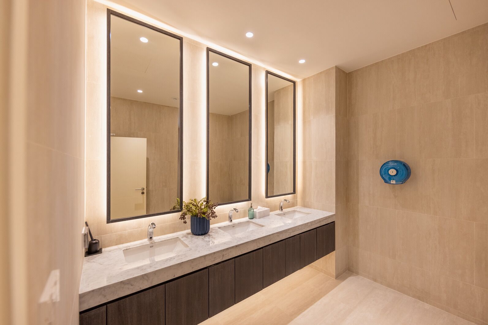 Un baño moderno con tocador doble, tres espejos y un calentador de agua azul.