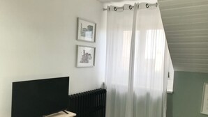 A room with a bed, a TV on a stand, a radiator, and two framed pictures on the wall. - Gîte Maison Chiche (Bain-de-Bretagne)