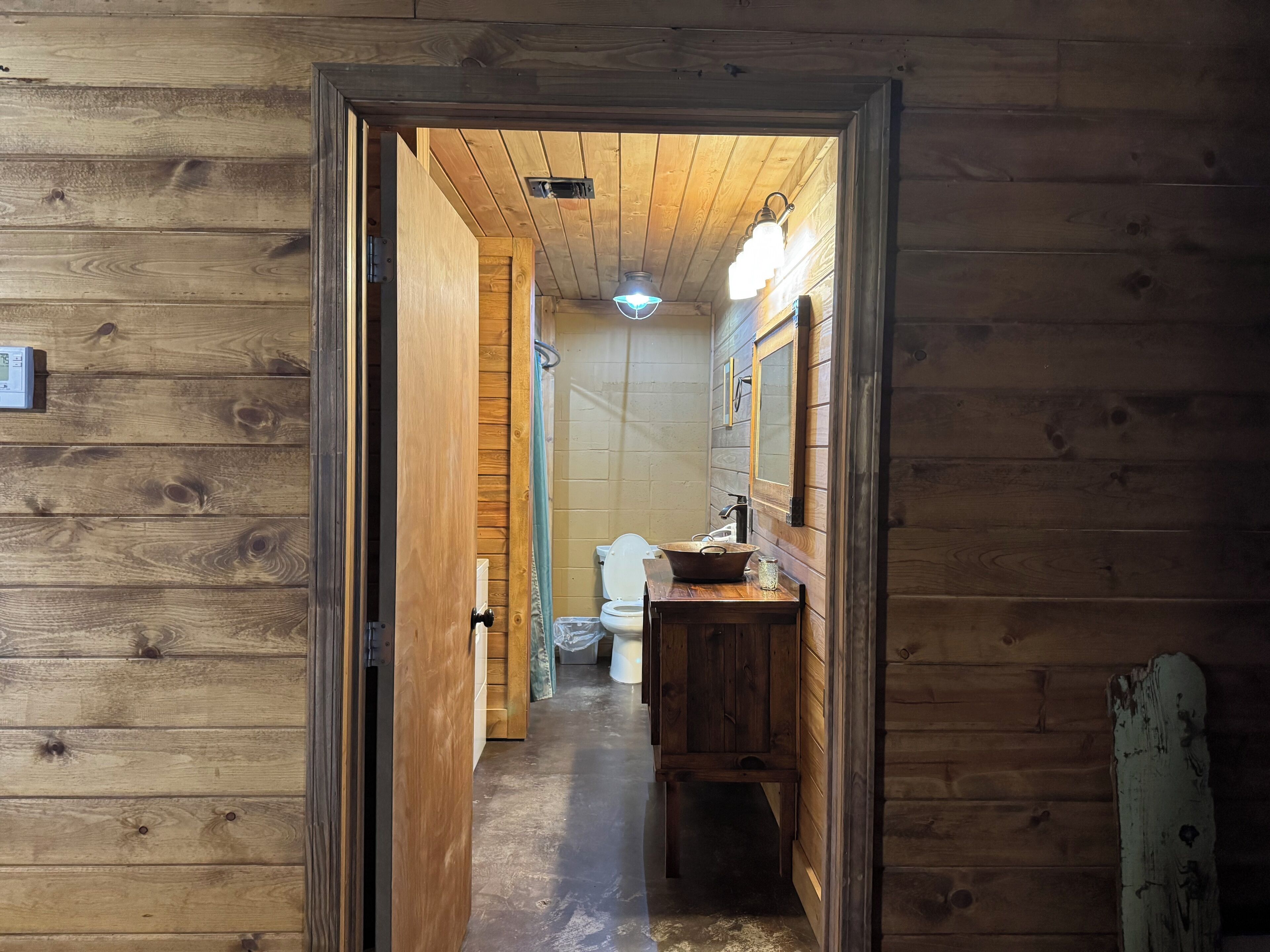 Pasillo interior de madera que conduce a un baño con lavamanos y espejo.