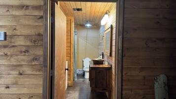Pasillo interior de madera que conduce a un baño con lavamanos y espejo.