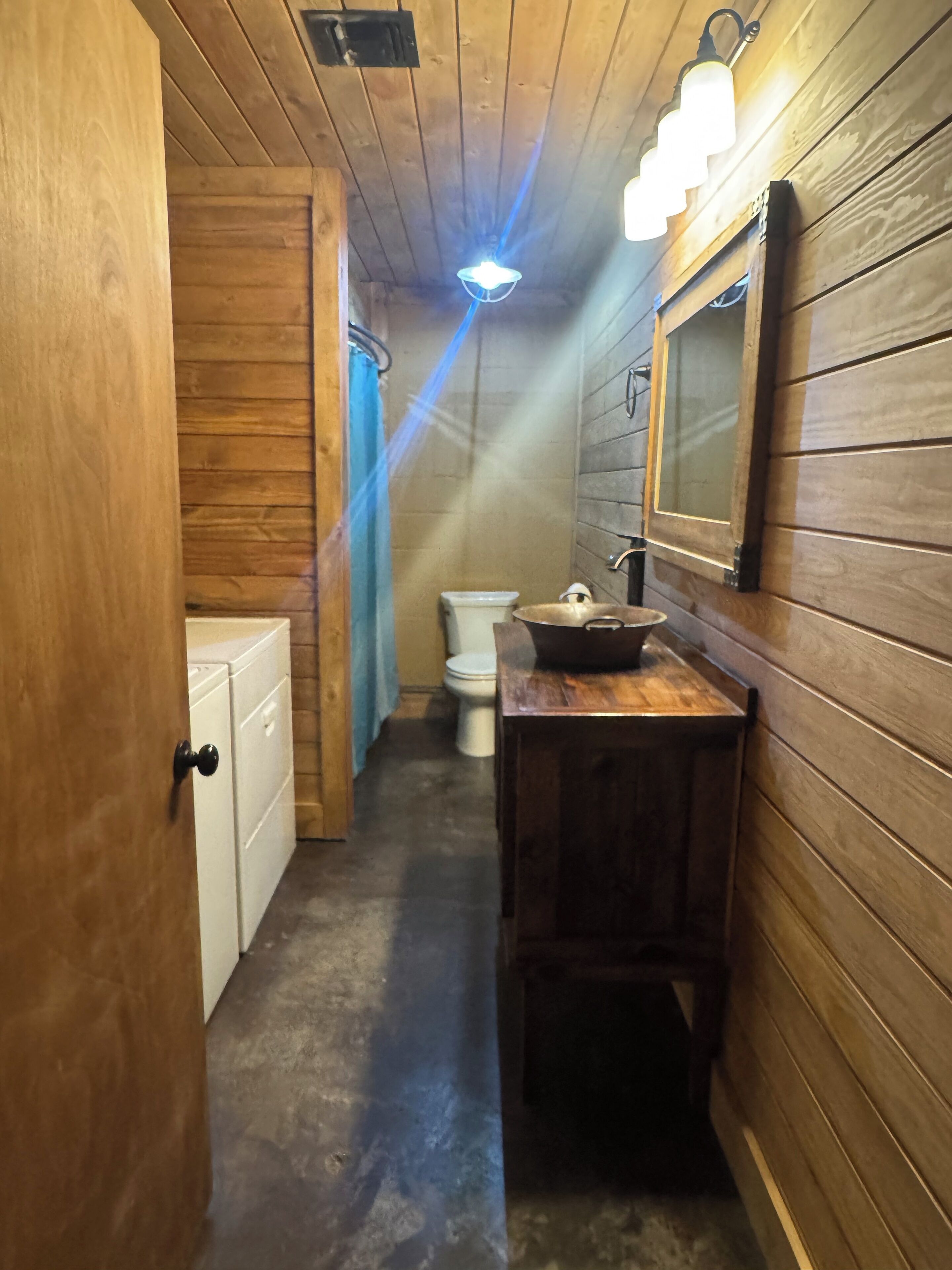 Un estrecho pasillo de madera que conduce a un baño con inodoro, lavamanos y un espejo en la pared.