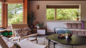 Una sala de estar acogedora con techo de madera, un sofá, una silla, una mesa y una ventana con vistas a la naturaleza.