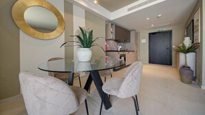 Un comedor moderno con una mesa de vidrio y sillas acolchadas, un espejo grande y una planta en maceta.