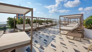 Terraza en la azotea con tumbonas y suelo estampado, con vistas a un paisaje urbano.