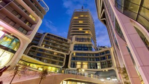 Um edifício moderno e imponente com várias varandas e grandes janelas, cercado por outros edifícios contemporâneos.