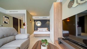Uma sala de estar moderna com um sofá, uma mesa de centro com uma planta, uma televisão e uma cama com cabeceira e almofadas.