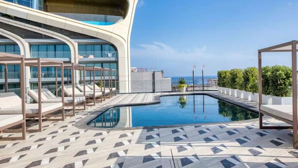 A rooftop pool area with lounge chairs and a modern building in the background. - The Official Mercury Suite With Pool & Strong WIFI (St. Julian`s)