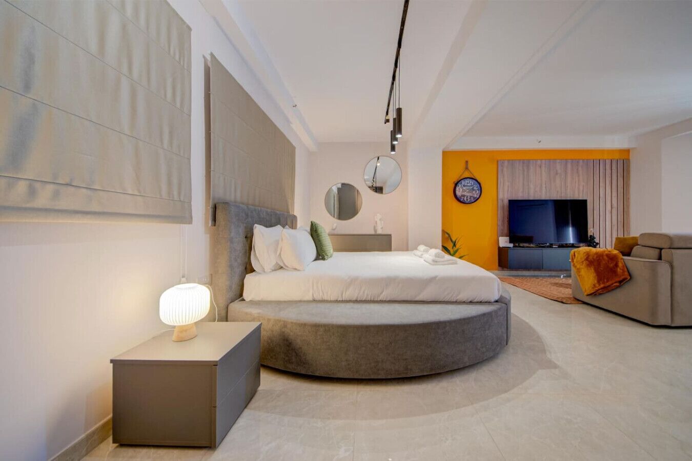 Un dormitorio moderno con una cama redonda, una mesita de noche, un sofá y un televisor.