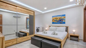 Quarto moderno com um espelho grande, uma cama com estrutura de madeira, uma mesinha de cabeceira pequena e um ar condicionado fixado na parede.