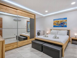 A modern bedroom with a large mirror, a bed with a wooden frame, a small bedside table, and a wall-mounted air conditioning unit.
