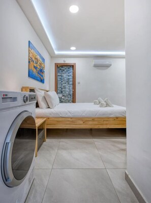 A compact bedroom with a bed, a washing machine, and a painting on the wall.