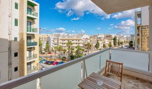 A balcony with a view of a cityscape, a table, and a chair.