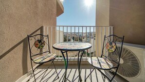Un balcon avec une table ronde et deux chaises, une balustrade blanche et une vue sur le paysage urbain.
