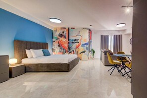 A modern hotel room with a large bed, a desk with chairs, and a colorful mural on the wall.