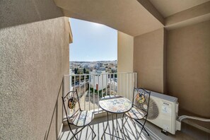 A balcony with two chairs and a table, a radiator, and a view of a cityscape.