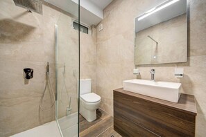 A modern bathroom with a glass-enclosed shower, a white toilet, and a wooden vanity with a white sink.