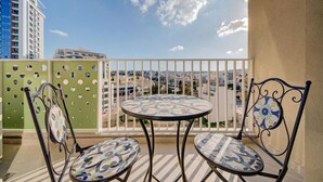 A balcony with two chairs and a table, overlooking a cityscape with buildings and a clear sky.