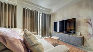 A modern hotel room with a large bed, a seating area, a flat-screen TV, and a small side table.